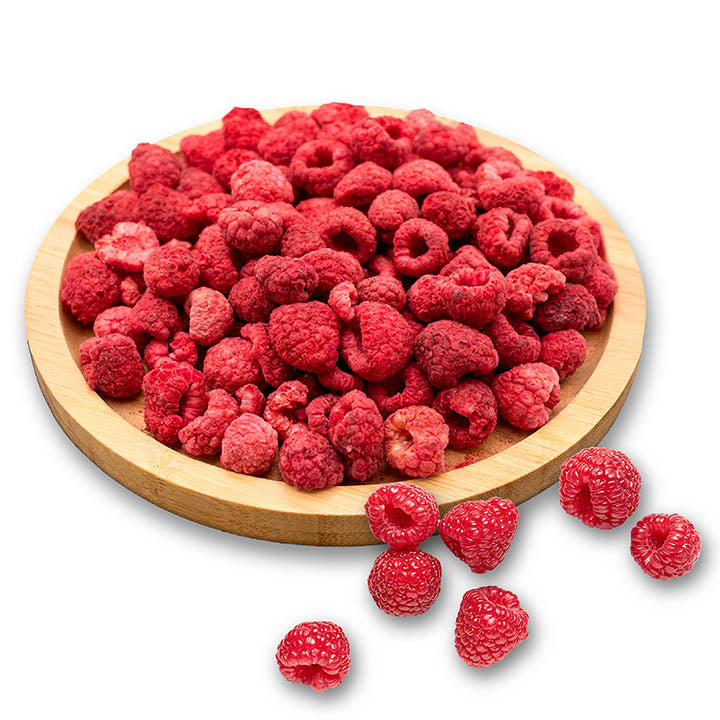 Dried raspberries on a wooden plate with some scattered on a white background