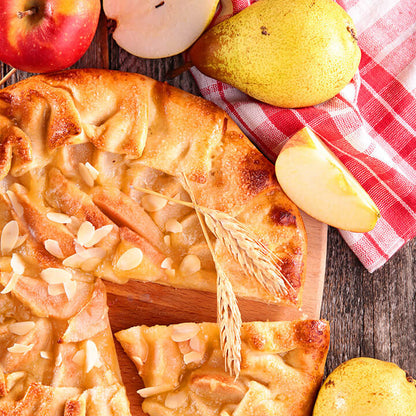 A baked apple pie with freeze dried sliced pieces on a wooden board, surrounded by whole and sliced apples, pears, and a red-and-white checkered cloth on a rustic wooden surface.