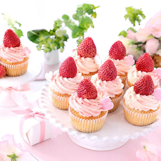 Cupcakes with pink frosting and strawberries on a decorative stand with flowers in the background.