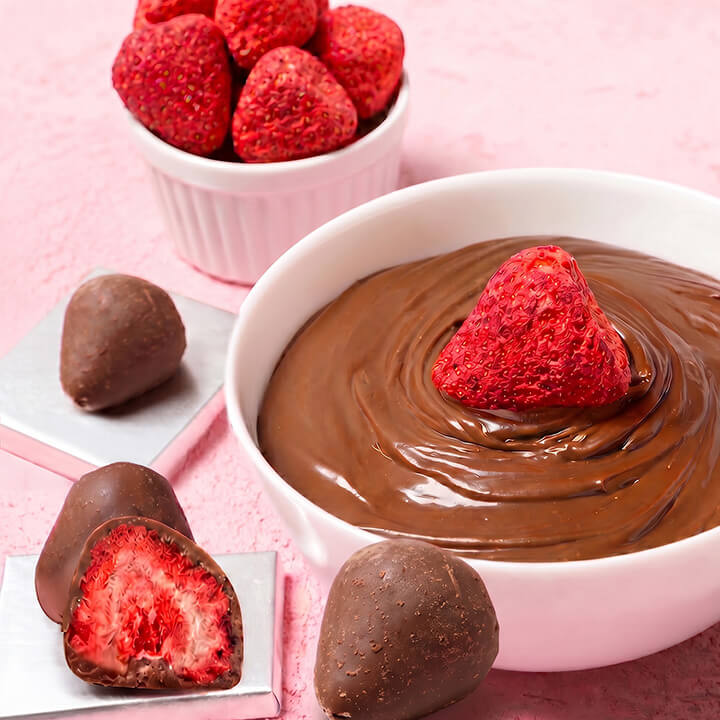 Bowl of chocolate with a strawberry, surrounded by chocolate-dipped strawberries on a pink background.